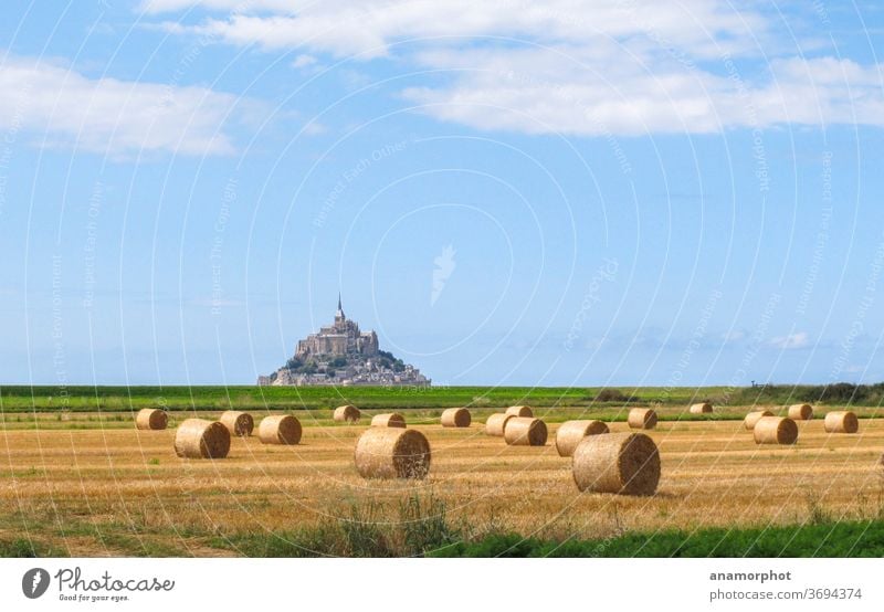 Rolls of straw on a field, Mont St. Michel in the background France Brittany Summer Sun Bale of straw Grain harvest Blue sky Yellow green Clouds in the sky