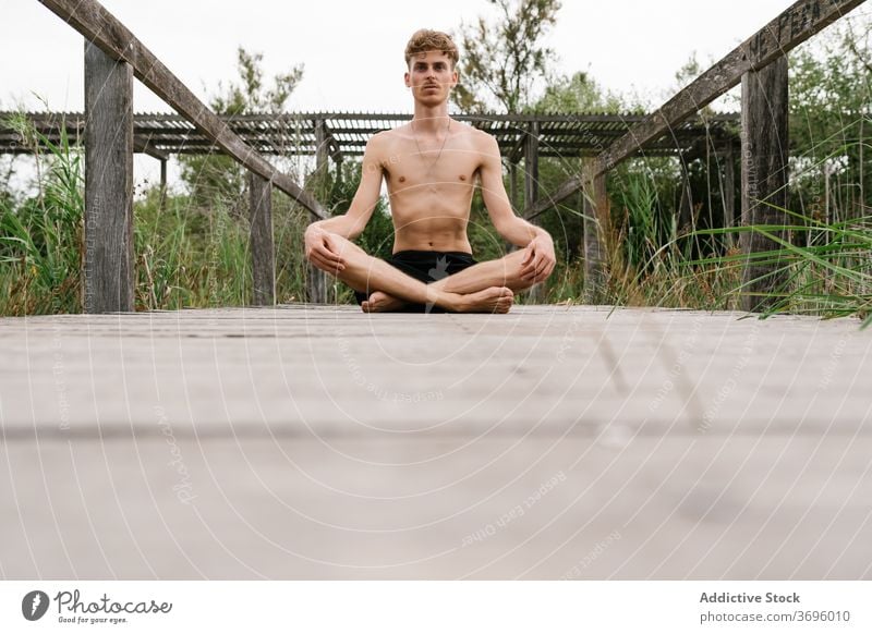 Man meditating in Lotus pose meditate lotus pose man yoga mindfulness stress relief nature tranquil harmony calm male wooden promenade healthy practice sit