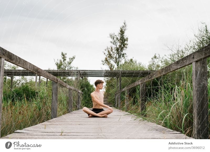 Shirtless man doing yoga on terrace padmasana practice flexible nature calm male pose harmony concentrate zen wooden healthy relax wellness balance stretch