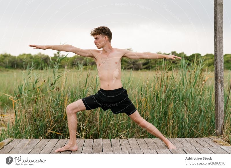 Flexible man doing yoga in warrior two pose practice flexible peaceful harmony nature terrace male healthy tranquil balance body vitality wellness calm wooden