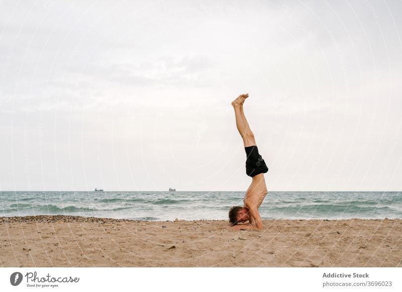 Young man in Forearm Balance yoga pose on beach practice sand asana forearm stand pincha mayurasana advanced balance inversion male young yogi slim shirtless
