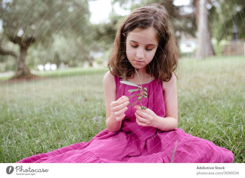 Calm little girl sitting on green grass summer park nature tranquil calm pensive kid adorable preteen female pink colorful dress child childhood charming relax
