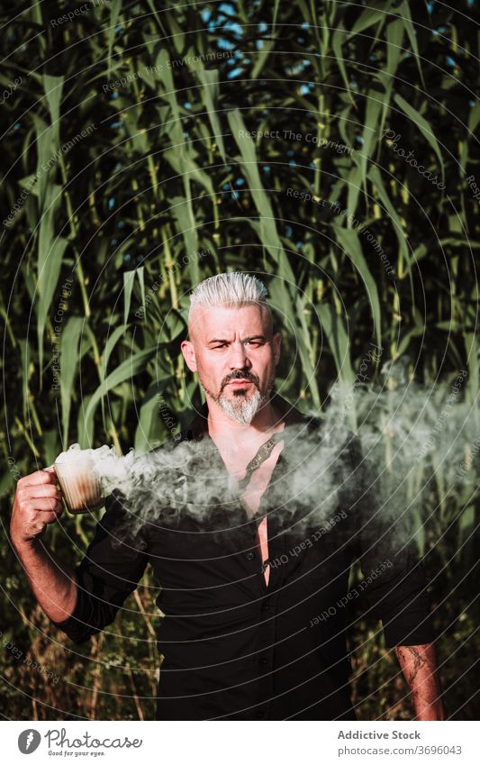 Mature bearded man with smoke bomb standing in field brutal serious confident determine strong portrait adult male tattoo gray hair middle age nature