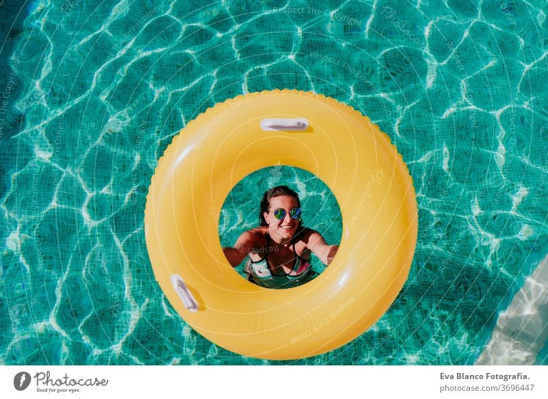 top view of happy young woman in a pool holding a yellow donuts. summer and fun lifestyle inflatable swimming bubbles caucasian dive clear health light water