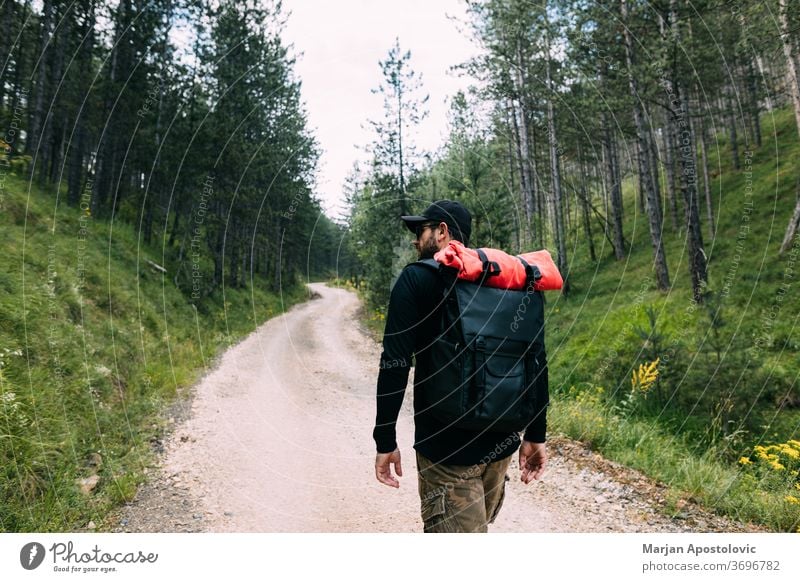 Young male nature explorer walking on the dirt road through the forest active adventure backpack backpacker backpacking countryside gravel green healthy hike