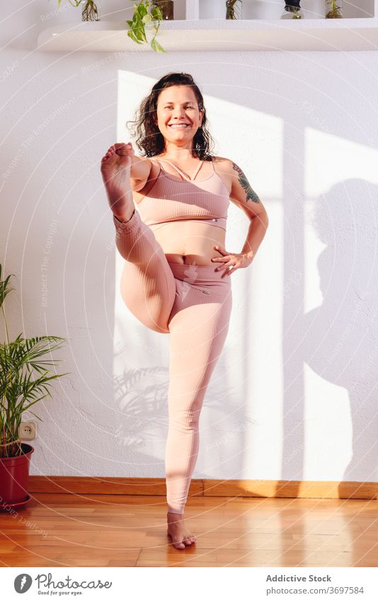 Smiling woman doing yoga in Standing Hand to Toe pose practice hasta padangusthasana hand to toe pose sportswear plump cheerful recreation female home smile