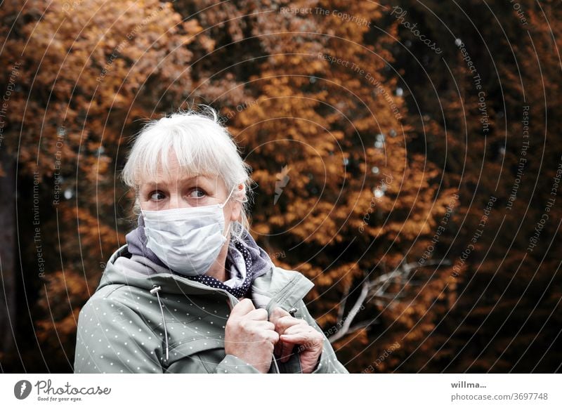 Blonde woman with medical mask looks skeptical - fear of infection Woman Mask risk of contagion corona Autumn anxiously asking cautious Senior citizen