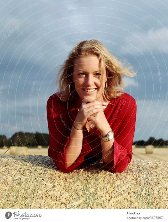 Portrait of a young woman on a bale of straw in the evening light Young woman Woman Blonde Freckles smile Red portrait Jewellery already Long-haired Upper body