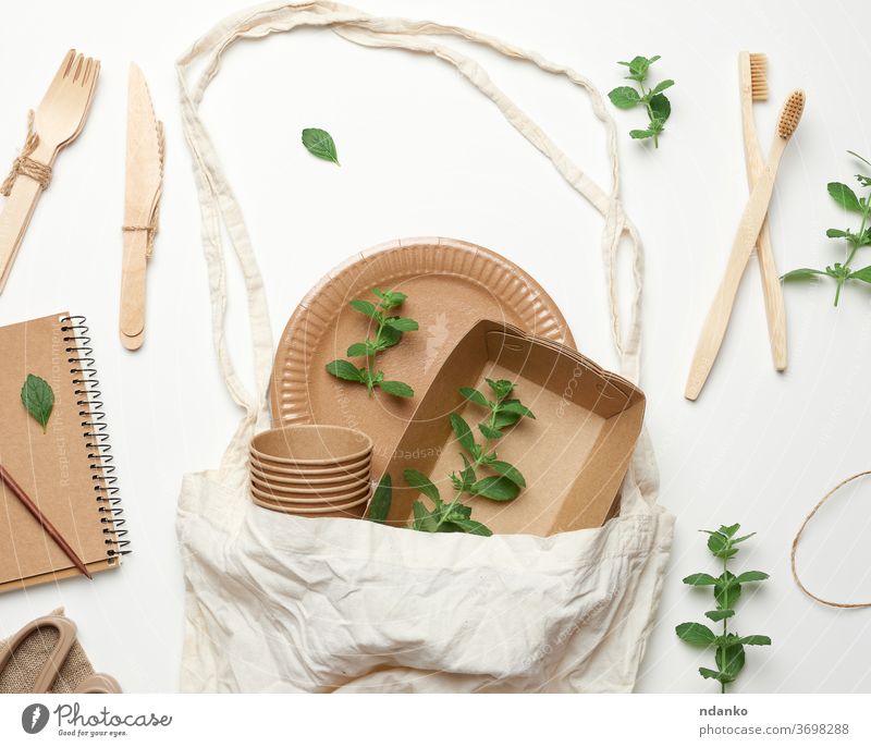 textile bag and disposable tableware from brown craft paper, green mint leaves on a white background. View from above, plastic rejection concept, zero waste