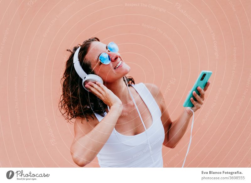 young happy woman outdoors listening to music on headset and mobile phone. Lifestyle at the city. Summertime. close up view music headset urban sunglasses