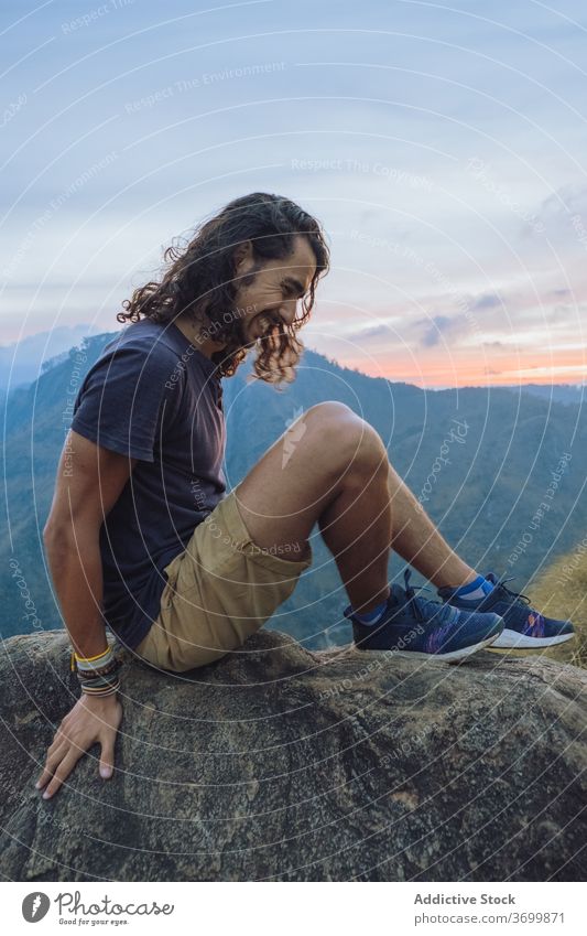 Man sitting on edge of mountain rock admiring views traveler sunset cheerful man admire landscape amazing happy male sri lanka journey nature smile adventure