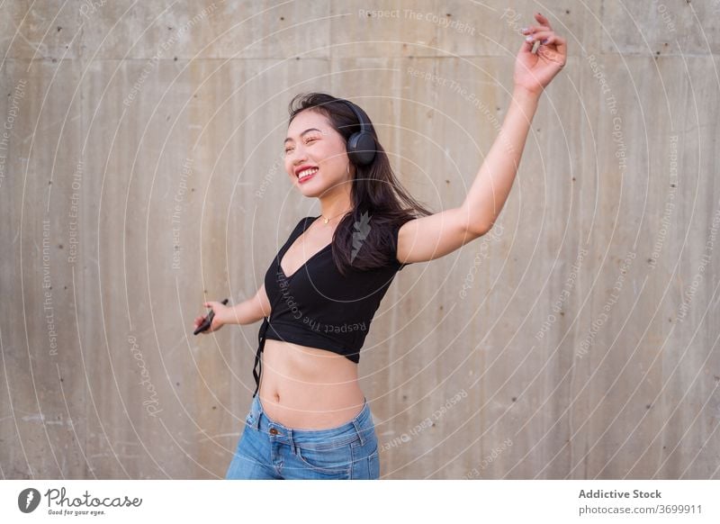 Carefree woman listening to music in headphones dance street carefree smartphone using enjoy female ethnic asian happy cheerful sound modern gadget device young