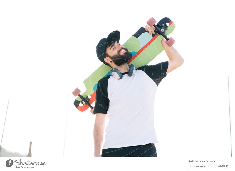 Smiling man with longboard on street hipster weekend city skater young generation sunny male summer smile joy relax trendy carefree cheerful urban cool beard