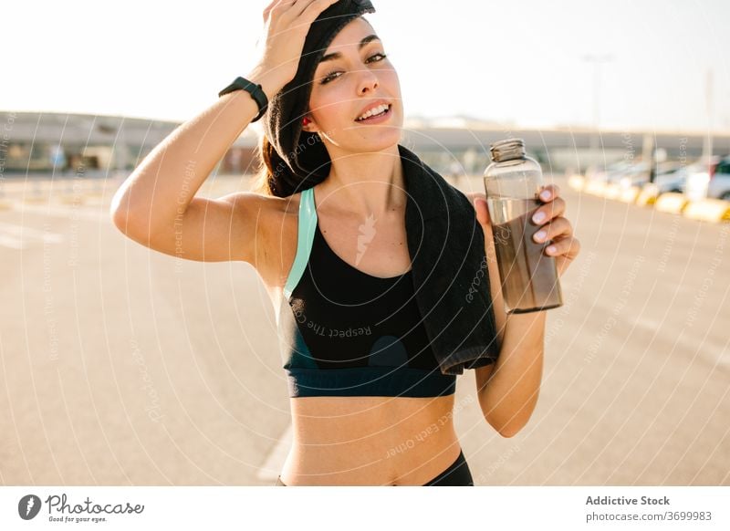 Tired sportswoman with bottle of drink on street tired sweat exhausted rest fit positive active training refreshment energy sporty young female hydrate beverage