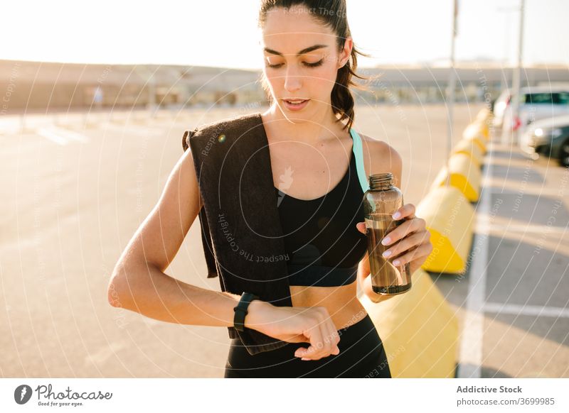 Young sportswoman checking fitness tracker after training on street bracelet app slim drink water rest using equipment active young sporty bottle hydrate