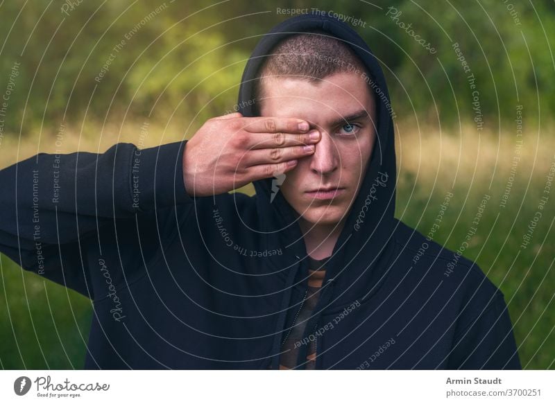 Portrait of a young man with a black hoodie covering his eyes portrait serious hand finger look teenager looking male beautiful casual caucasian outdoor