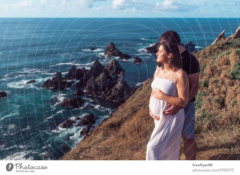 Pregnant couple on top of a cliff near the ocean pregnant cliffs holding belly expecting pregnancy copy space baby mother gestation woman maternity motherhood