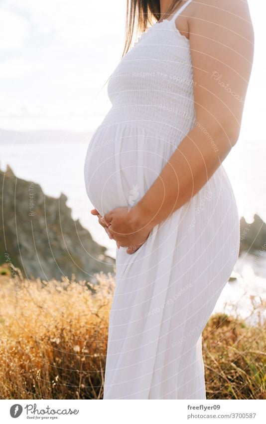 Detail of a pregnant body from the side pregnancy copy space holding hands care expecting belly baby reproduction mother white dress gestation one woman