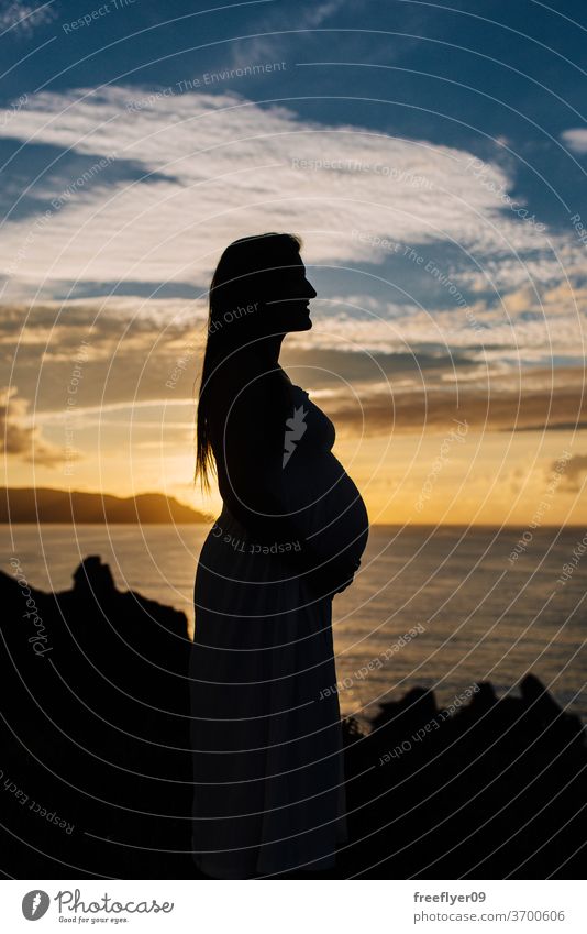 Silhouette of a pregnant woman against an oceanic landscape silhouette profile side view copy space dark black backlighting sunset sunlight light effect