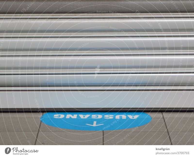 Blue sticker with white writing "AUSGANG" and white arrow on the floor in front of a closed shop Way out Signs and labeling Signage Characters Arrow Direction