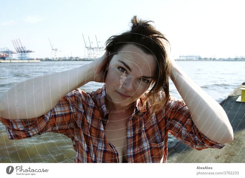 Young woman with freckles sitting on a pontoon in front of Hamburg harbour portrait Central perspective Looking brunette hair Copy Space right freckly Joy Model