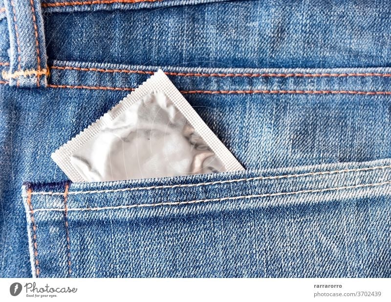 A condom pops out of the front pocket of a pair of jeans texture cotton fabric protection pack safety blue healthy contraceptive man latex hiv risk sex
