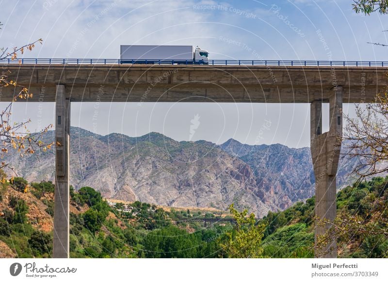 Truck with refrigerated semi-trailer crossing a viaduct with a landscape of mountains in the background truck bridge road trayler transportation highway travel