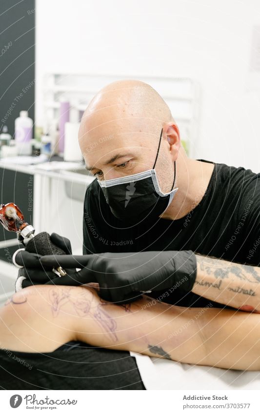 Male master doing tattoo in salon tattooist machine client professional art body table lying equipment artist work style creative ink studio contemporary