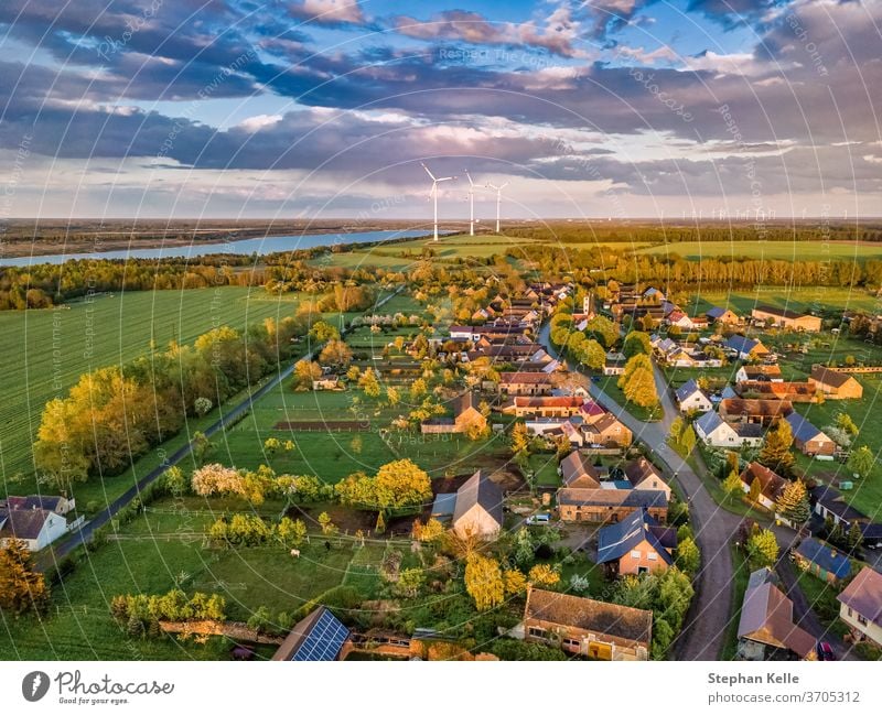Aerial view over a little town with wind wheels and a lake in the background of a german countryside. village clouds drive high landscape nature electricity sun