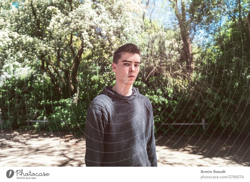 Portrait of a serious young man in a park cool casual sunlight sunbeam outdoors perspective trendy confident portrait teenager looking male beautiful caucasian