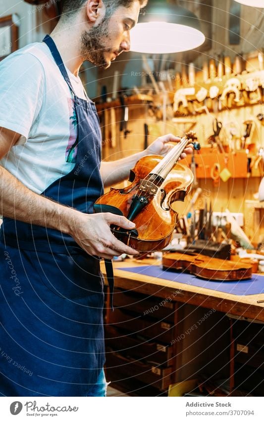 Male master in workshop with violins man repairman instrument music craftsman workbench apron male shiny equipment modern hobby tool focus table professional