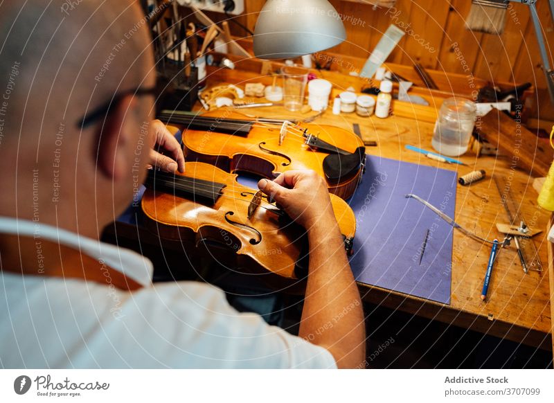 Luthier adjusting violin bridge in workshop repair craftsman artisan string instrument luthier restore skill master male maker handmade occupation professional