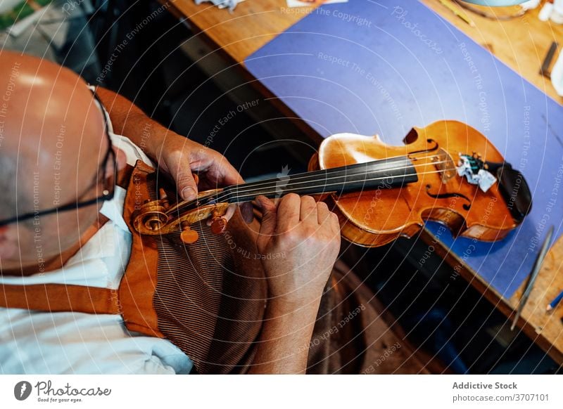 Craftsman with violin in professional workshop craftsman repair luthier artisan restore master skill male mature middle age maker handmade occupation workplace