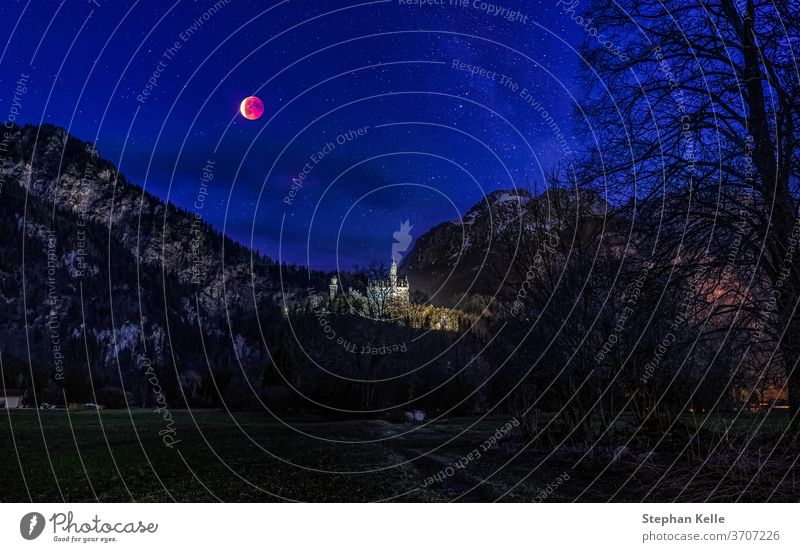 Bloody moon over a castle with mountains in background in germany at the night sky. bloody stars composing alps landscape nature full luna illuminated road
