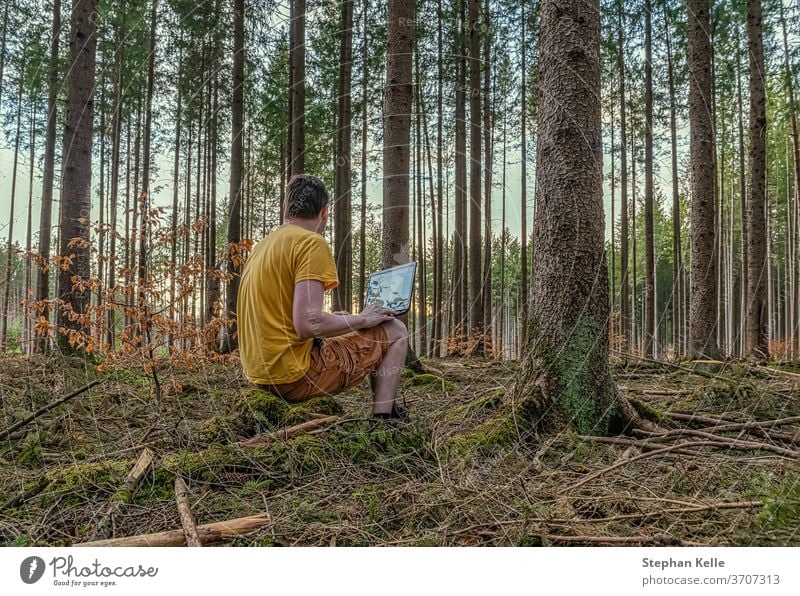 Enjoying work on the fresh air, a man works with his laptop in a natural looking forest. working modern cozy office free health computer concrete green