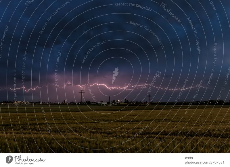 Thunderstorm atmosphere with lightning over wheat fields with cloudy sky and view of Inningen near Augsburg View copy space dark gigantic gloomy landscape