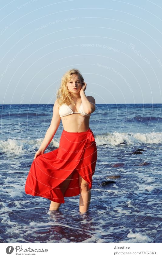 Portrait of a young blonde woman with red skirt and bikini top in the Baltic Sea Young woman Woman girl 18-20 years Blonde Slim already Curly sensual natural