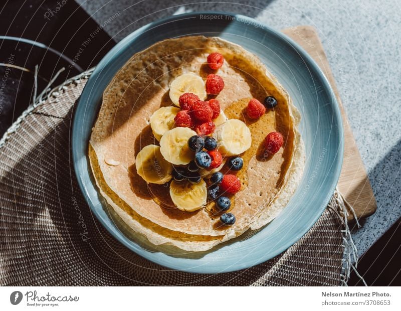Overview of a delicious crepe with bananas, blueberries, raspberries and honey. It is lit with a nice natural light in the kitchen. food sweet healthy fruits