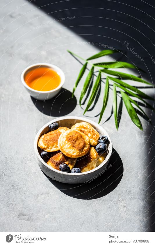 Mini pancakes with fresh blueberries and honey on a grey background. Shadows and light. Small Honey Breakfast Roasted Hot dressed bowls Drop shadow Light