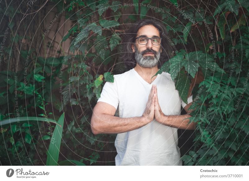 Man in white with long gray hair and glasses standing on a garden with his hands together in meditation hindu chakra meditating pray meditate balance pose man
