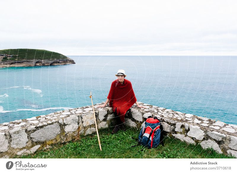 Stylish traveling woman with backpack resting near sea hiker backpacker traveler pilgrimage style trekking stone seaside camino de santiago cliff spain sit