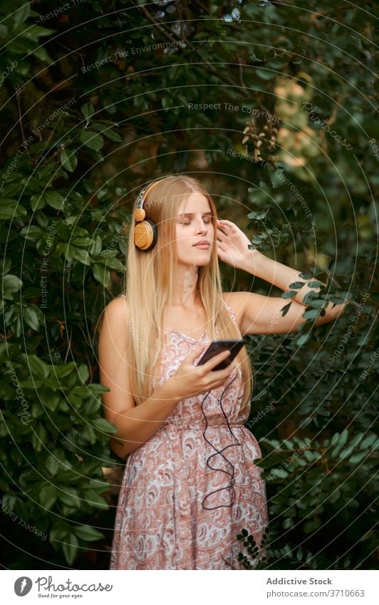 Calm young woman listening to music in garden smartphone headphones serene relax calm enjoy blond female technology summer foliage happy gadget device lifestyle