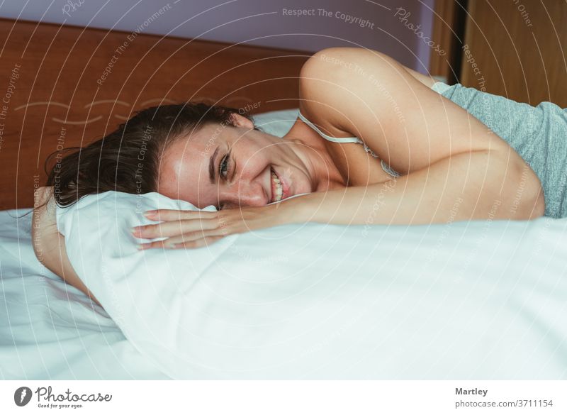 Close up portrait of a smiling attractive woman lying down on bed and looking at the camera. people adult one girl room bedroom family brunette at home