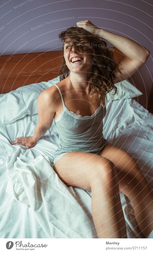 From above young woman sitting on bed with eyes open and hair on her face and laughing in morning. beautiful stay at home bedroom lifestyle pajamas pretty
