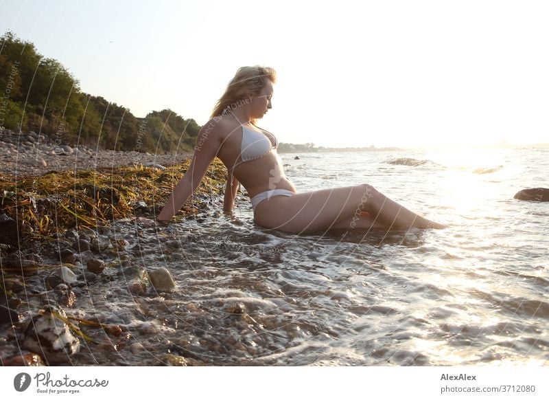 Portrait of a young blonde woman in a bikini, sitting in the Baltic Sea surf Young woman Woman girl 18-20 years Blonde Slim already Curly sensual natural