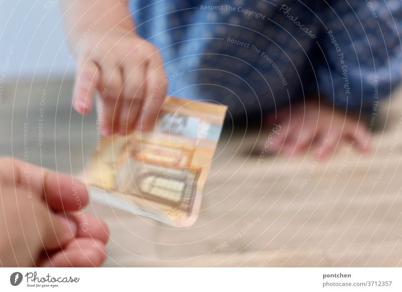 Children cost money. A 50 Euro note changes from the hand of an adult to the hand of a child. Giving money, spending money. Costs. Child benefit. Family allowance.