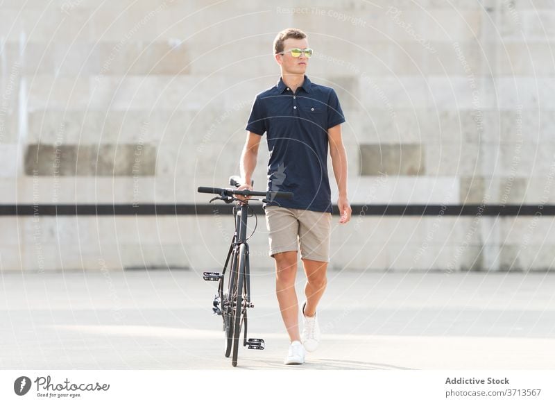 Young man with bicycle on the street adult bike blond casual caucasian copy space ride cycling cyclist lifestyle male millennial mobility modern people riding