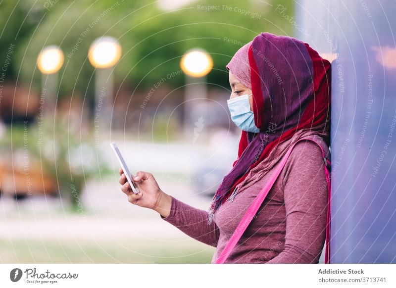 Sportive woman in mask using smartphone on street sportswoman city hijab medical coronavirus sportswear female arab ethnic building browsing cellphone online