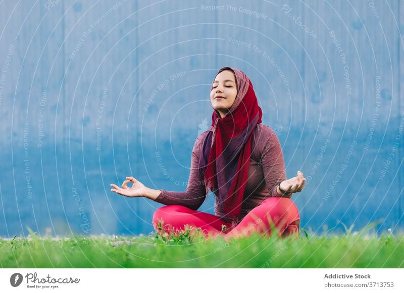 Muslim woman meditating in Lotus pose meditate yoga lotus pose park practice asana mindfulness stress relief padmasana female arab ethnic hijab muslim