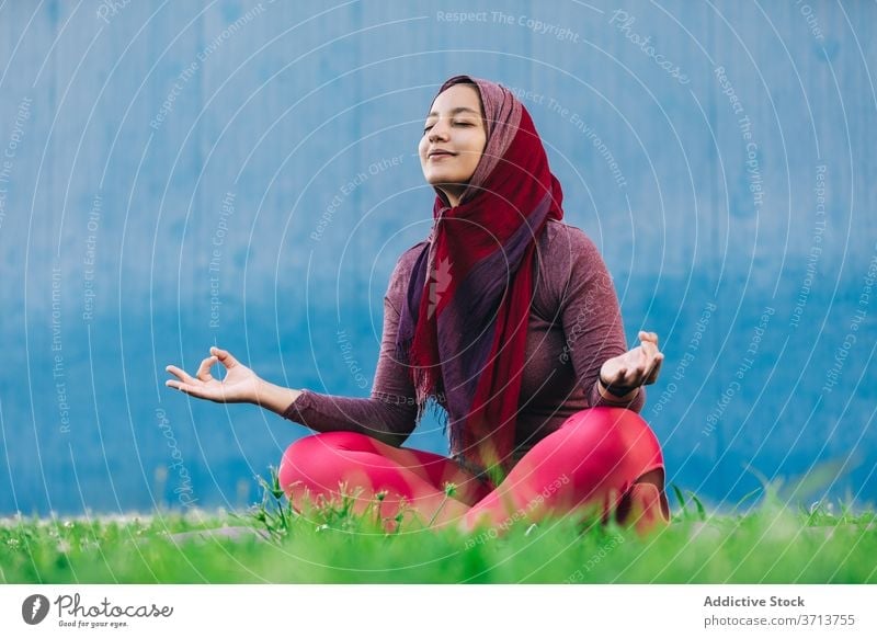 Muslim woman meditating in Lotus pose meditate yoga lotus pose park practice asana mindfulness stress relief padmasana female arab ethnic hijab muslim